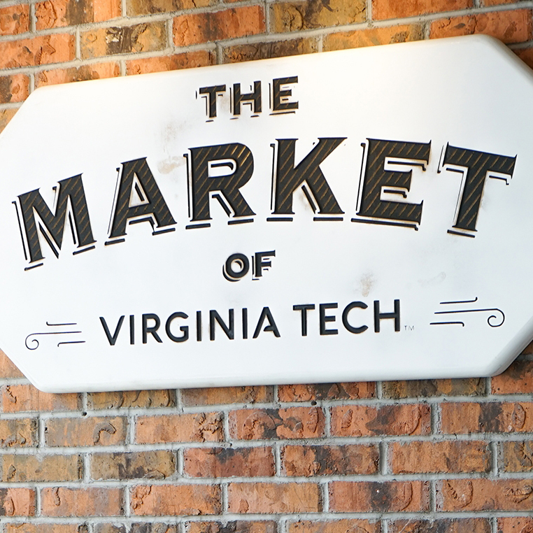 a sign, with the market of virginia tech logo on it, hanging on a wall