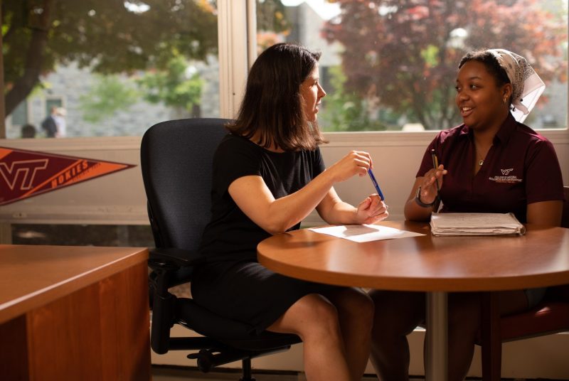 Advising Center Assistant Director Dana McGuire sits at a table and talks with a female student in her office. 
